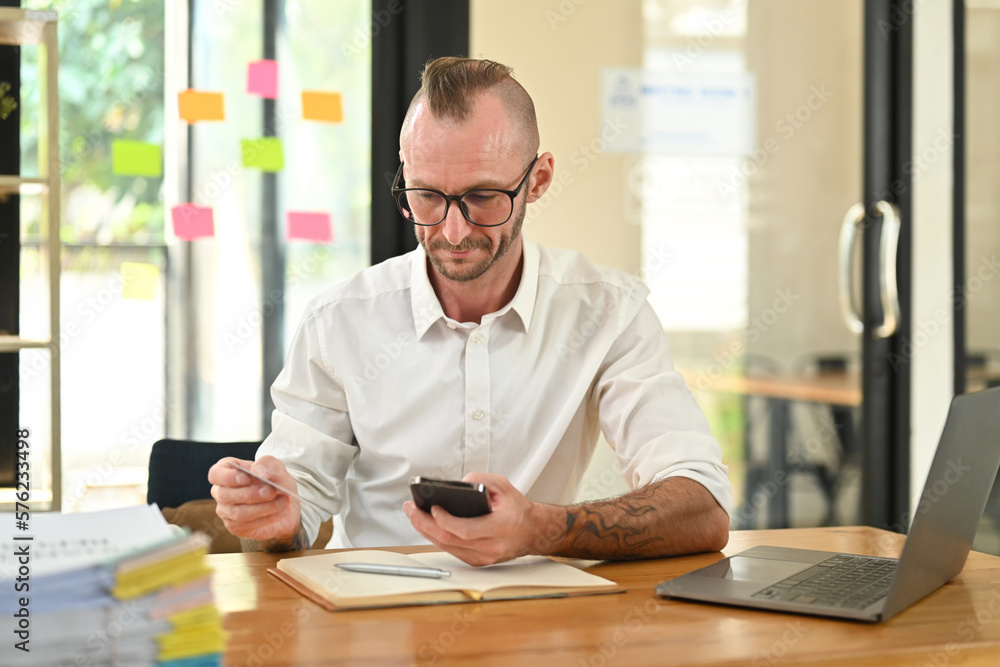 Pleasant caucasian male consumer holding credit card and smartphone, doing online banking transaction Pleasant caucasian male consumer holding credit card and smartphone, doing online banking transaction