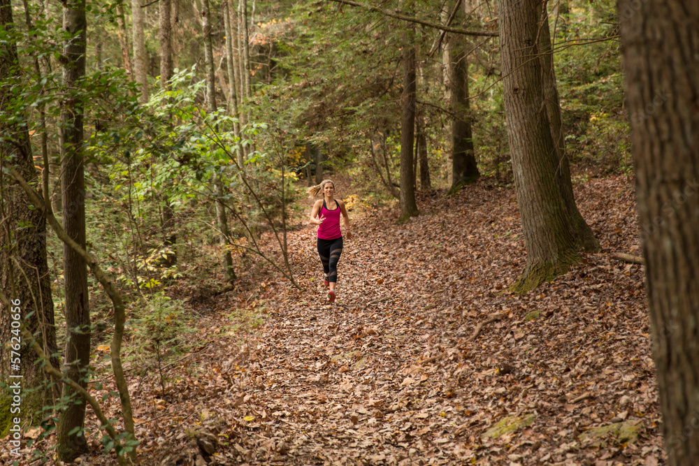 A young blonde woman runs on a trail in the forest in the fall