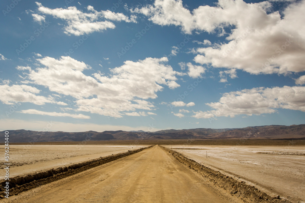 PANAMINT VALLEY, CA, USA. A long, desolate dirt road extends into a distant horizon under blue, cloudy skies. PANAMINT VALLEY, CA, USA. A long, desolate dirt road extends into a distant horizon under blue, cloudy skies.