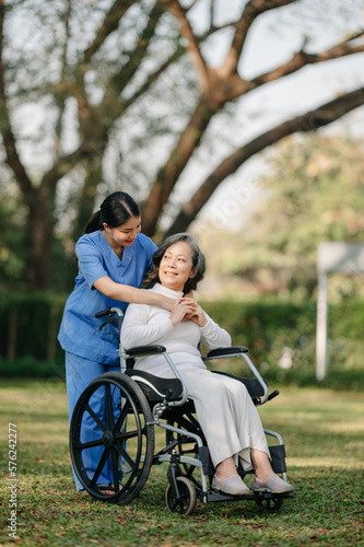 Elderly asian senior woman on wheelchair with Asian careful caregiver and encourage patient, walking in garden. with care from a caregiver and senior health insurance...