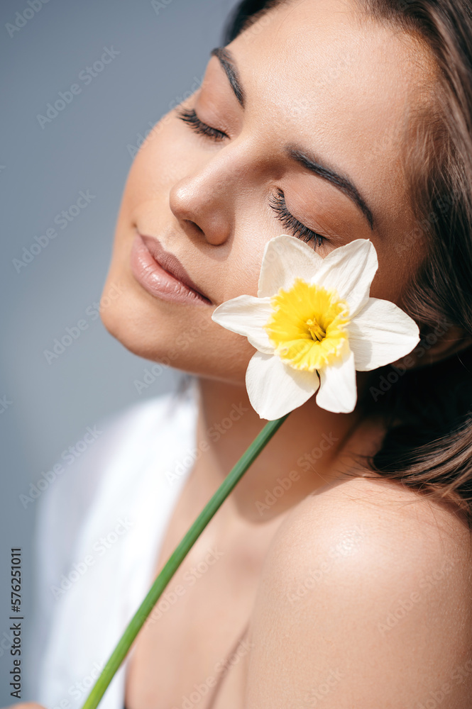 Tender millennial lady holding bunch of daffodils over grey studio background