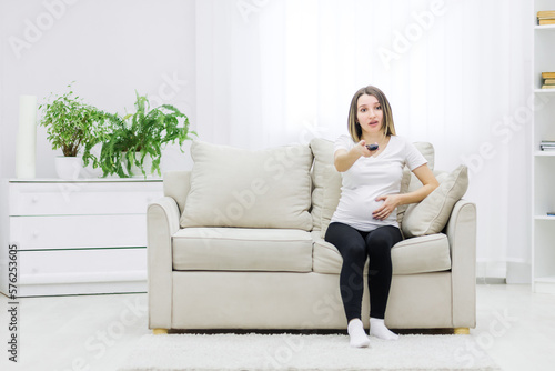 Pregnant woman facial expression sitting on sofa with remote control.