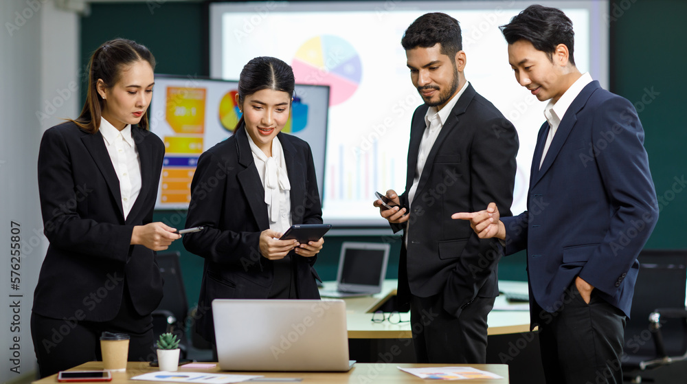 Millennial Asian Indian professional male businessmen female businesswomen employee staff colleagues in formal business suit standing discussing brainstorming working together with laptop computer Millennial Asian Indian professional male businessmen female businesswomen employee staff colleagues in formal business suit standing discussing brainstorming working together with laptop computer