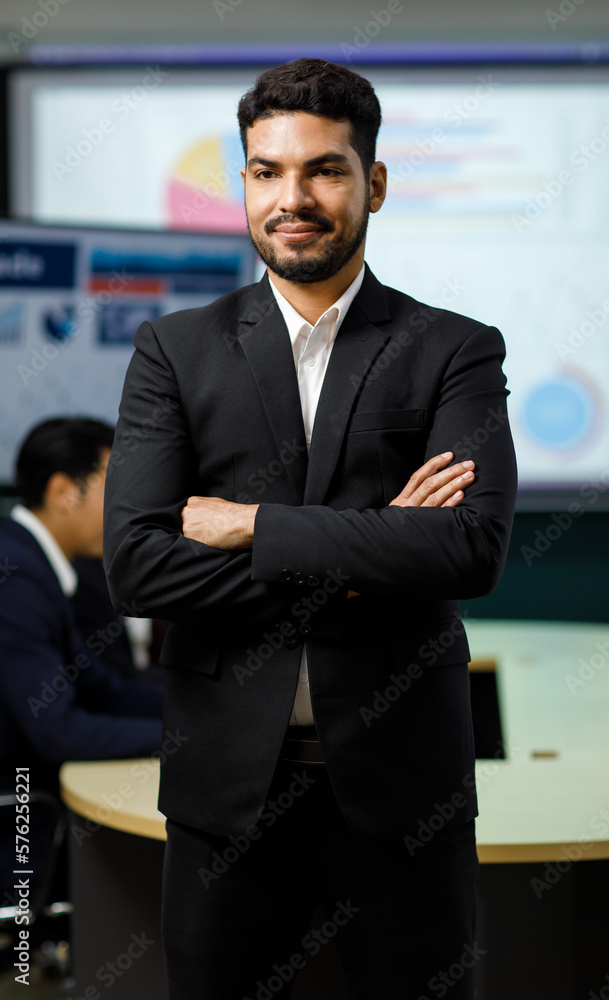 Millennial Asian Indian professional successful bearded male businessman entrepreneur ceo management in formal business suit standing smiling crossed arms portrait photo in company office meeting room Millennial Asian Indian professional successful bearded male businessman entrepreneur ceo management in formal business suit standing smiling crossed arms portrait photo in company office meeting room