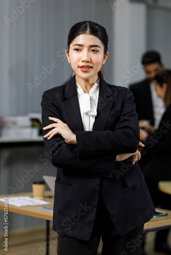 Millennial Asian professional successful female businesswoman entrepreneur ceo management in formal business suit standing smiling crossed arms posing taking portrait in company office meeting room