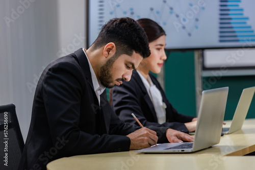 Millennial Asian professional female businesswoman audience in formal business suit sitting looking at laptop notebook computer screen in company office meeting room with Indian male businessman