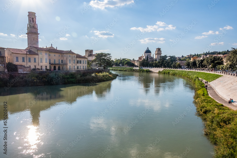 Calm waters of the Adige river which crosses Verona with gardens and a church with a bell tower
