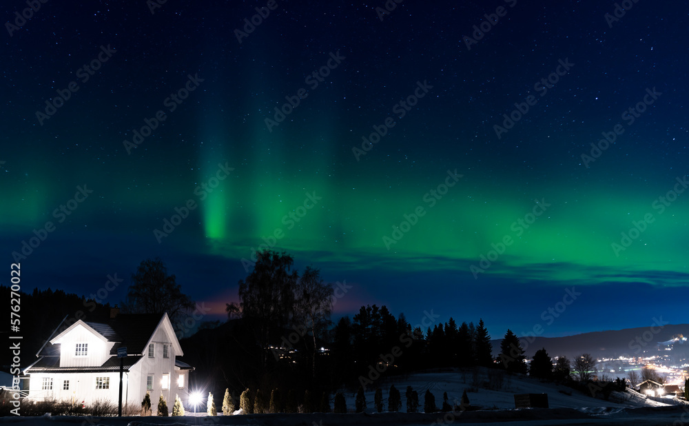 Northern lights in clear Green colors, rushing across a clear starry night sky. A small residential home in the foreground.