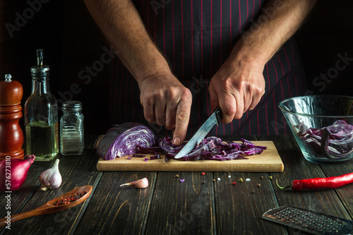 Cooking fresh red cabbage salad by the hands of the cook in the kitchen. Vegetarian food concept on dark background with place for recipe