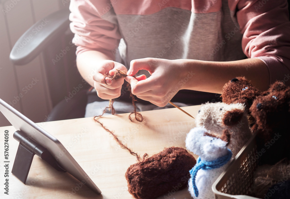 Obraz premium A young woman sits at a table and knits with her knitting needles, using a clipboard to learn.