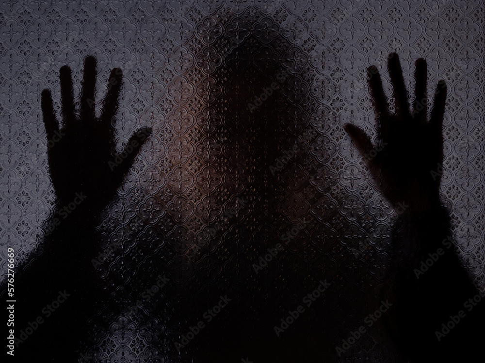 Blurred silhouette of a mysterious woman standing behind frosted glass with both hands against the glass. Concept of asking for help, loneliness or depression Blurred silhouette of a mysterious woman standing behind frosted glass with both hands against the glass. Concept of asking for help, loneliness or depression