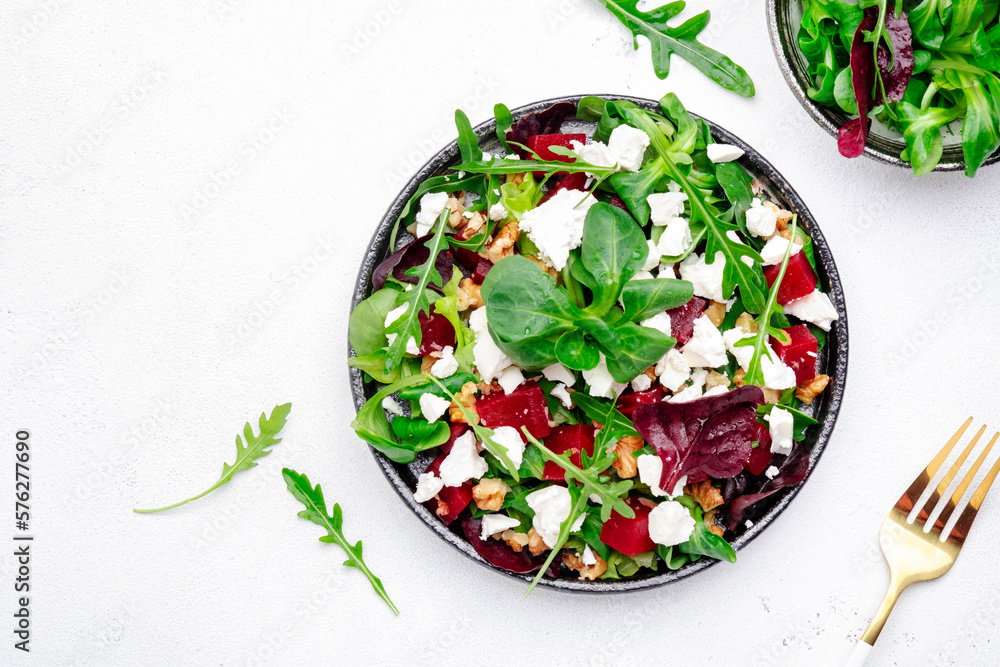 Beet and feta cheese healthy salad with arugula, lamb lettuce, mini chard and walnuts, gray kitchen table, place for text. Fresh useful vegan dish for healthy eating