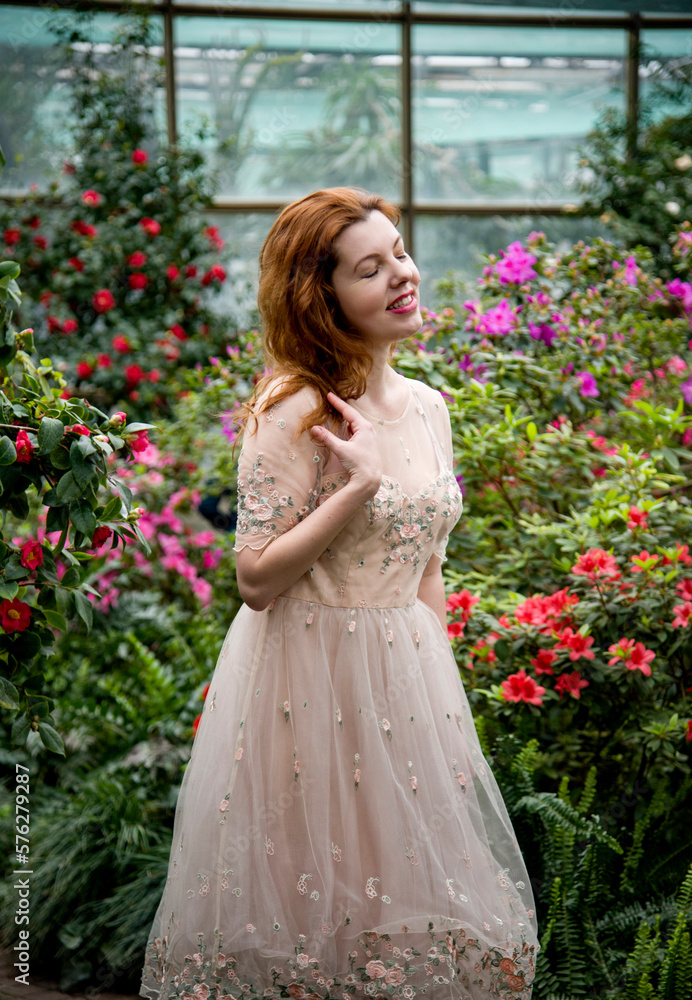 portrait of beautiful romantic redhead woman in pink dress walking with flowers in spring garden