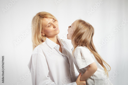 Portrait of a mother and daughter, where a little girl screams at an adult woman on a white background. The concept of a capricious child and behavior in the family. Angry teen and calm lady