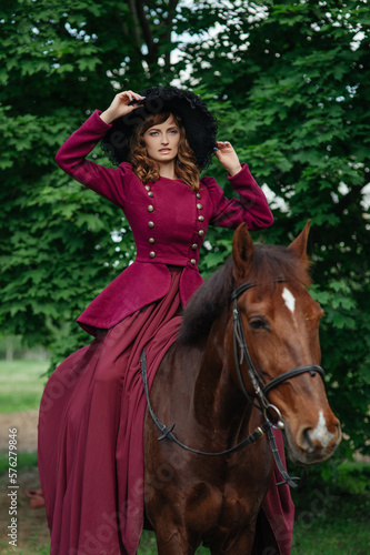 Beautiful elegant woman in lilac dress and hat rides cute horse. Horse riding. Horse lovers. Vintage portrait of aristocrat lady in old fashioned purple dress riding brown horse. Walk on horseback