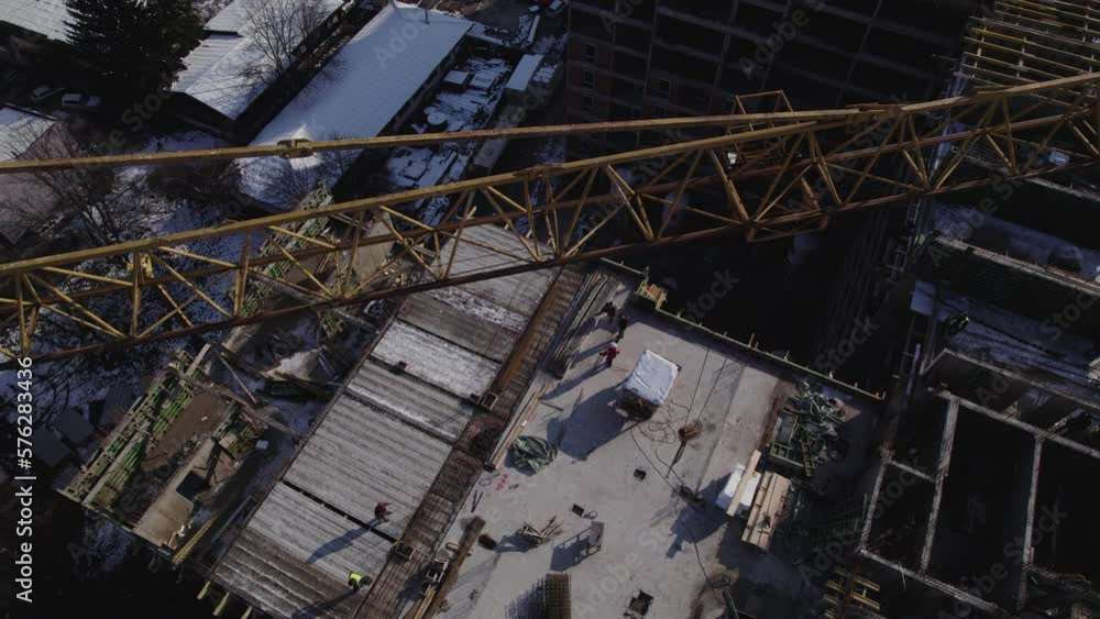 Overview of crane in a construction site with workers walking Overview of crane in a construction site with workers walking