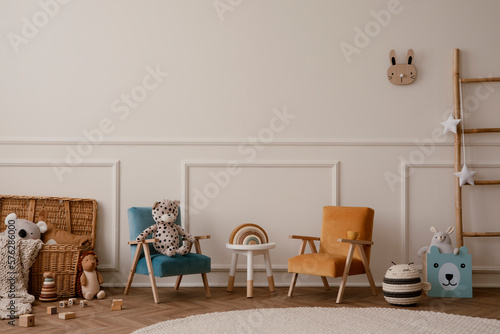Warm and cozy kids room interior with orange and beige armchair, white stool, round rug, plush toys, wooden blockers, beige wall with stucco, ladder and personal accessories. Home decor. Template.