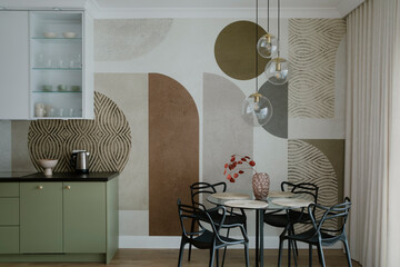 Interior design of dinning room interior with round glass table, stylish chair, green kitchen shelf, lamp, vase with dried flowers, patterned wallpaper and personal accessories. Home decor. Template.