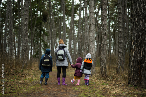 Back of mom and children with backpacks walking along the forest road after rain together. © AS Photo Family