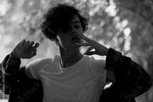 Defiant dark-haired teenager smoking outdoors in shadow of trees