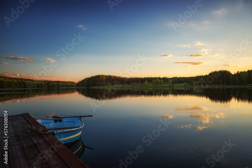 summer evening on the bank of a forest river, a place for fishing on a wooden bridge, and a boat