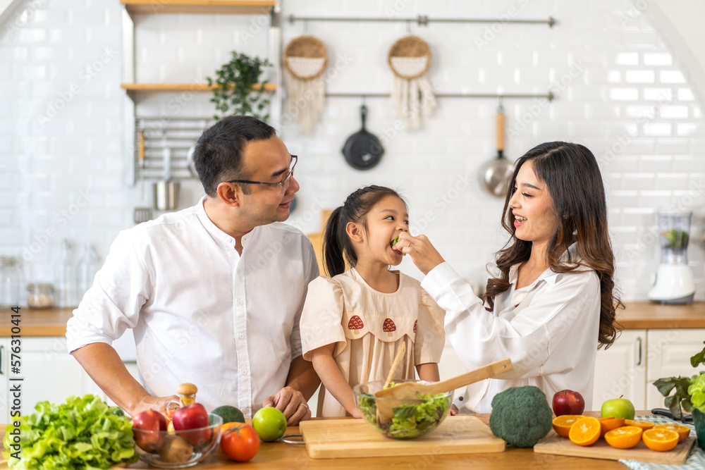 Portrait of enjoy happy love asian family father and mother with little asian girl daughter child having fun help cooking food healthy eat together with fresh vegetable salad ingredient in kitchen Portrait of enjoy happy love asian family father and mother with little asian girl daughter child having fun help cooking food healthy eat together with fresh vegetable salad ingredient in kitchen