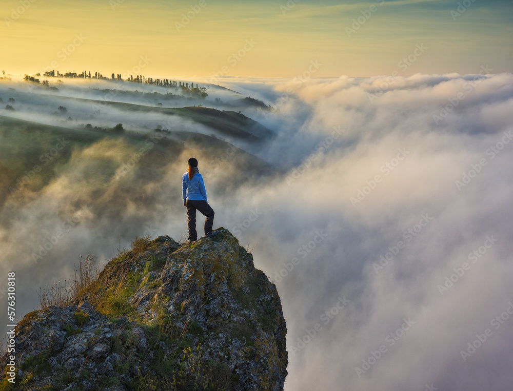Obraz premium young woman stands on a rock above a river canyon. female tourist enjoys foggy autumn landscape. nature of Ukraine