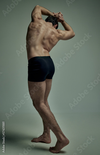 Healthy spine. Full-length image strong man with muscular body, relief back posing shirtless over pale green studio background. Concept of man's beauty, sportive and healthy lifestyle, fashion photo