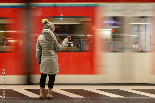 mulher com roupa de inverno na plataforma do metro segurando uma xicara de chá em quanto o trem passa borrado ao fundo  photo