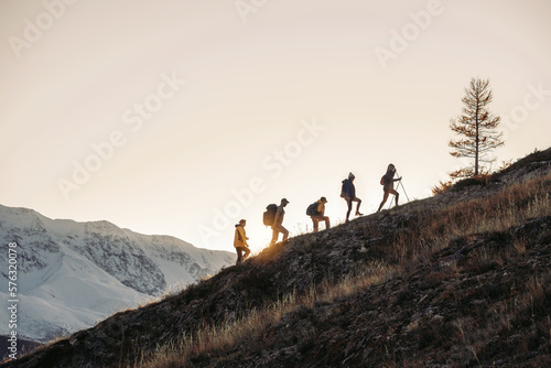 Fotografie, Tablou Group of tourists silhouettes walks with backpacks in mountains