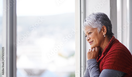 Lost in thought. Shot of a mature woman standing by a window on a sunny day.