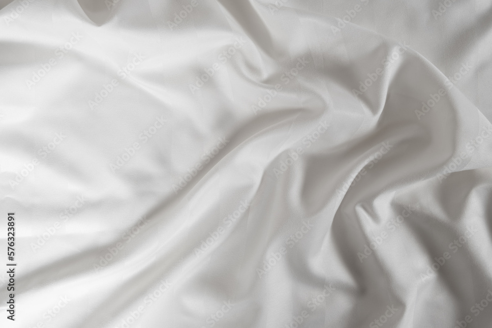 Satin crumpled fabric of white color, top view. Natural bed linen, sheets, abstract background of luxury fabric, wavy folds