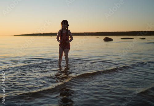 Little girl in a wet dress on the sea on a summer evening.