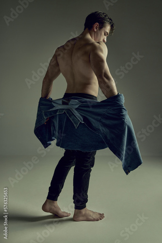 Round back. Full-length image. Male strong healthy body. Model posing with shirt in pants over pale green studio background. Concept of man's beauty, sportive and healthy lifestyle, fashion photo