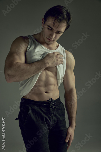 Portrait of young man with muscular relief body, torso. Male model posing in singlet over green studio background. Concept of man's beauty, sportive and healthy lifestyle, fashion, strength photo