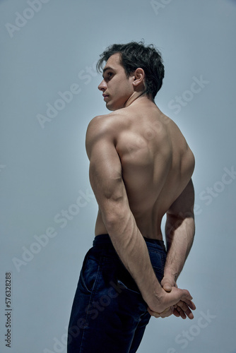 Relief, strong, healthy back. Muscular young man posing shirtless in underwear over blue studio background. Concept of man's beauty, sportive and healthy lifestyle, fashion, strength photo