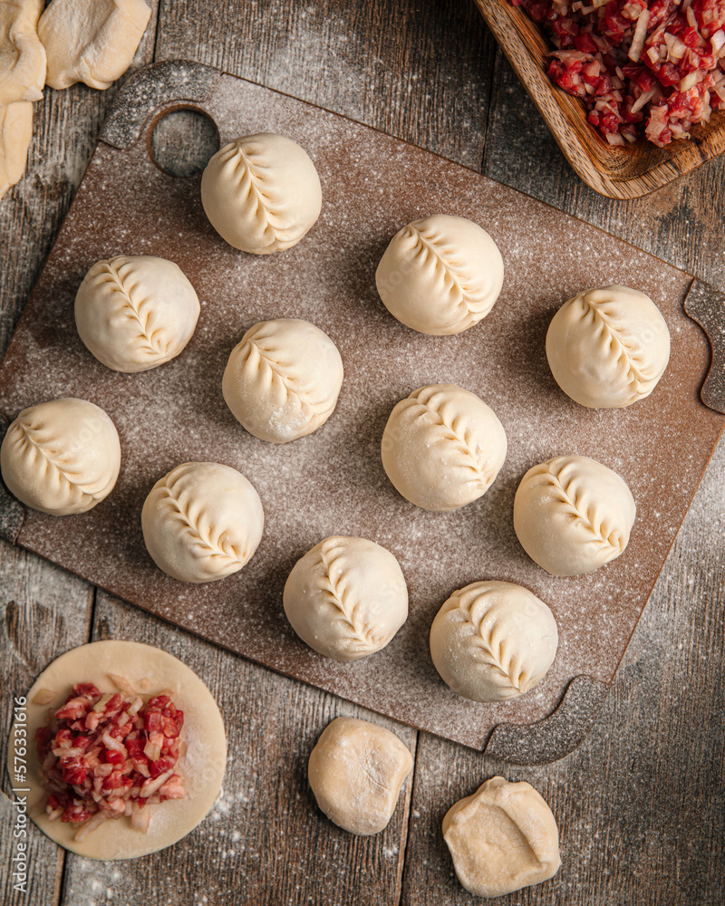 Semi-finished manti dumplings on wooden board with flour
