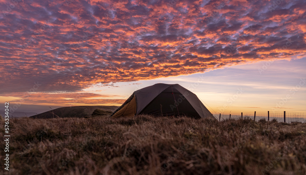 Beautiful wild camping scene with tent under gorgeous sunset clouds