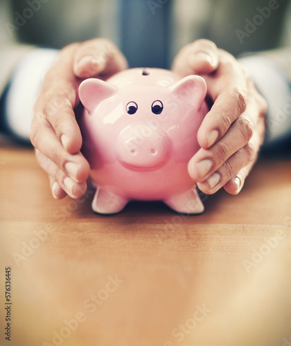 His assets are secure. Cropped image of a businessmans hands covering his piggybank.