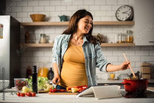Beautiful pregnant woman preparing delicious food. Smiling woman cooking pasta at home.