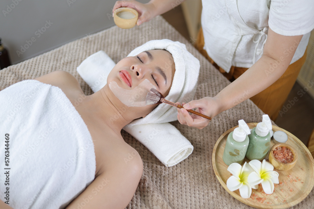 Young woman with nutrient facial mask in beauty salon. Face peeling mask, spa beauty treatment, skincare. Woman getting facial care by beautician at spa salon.