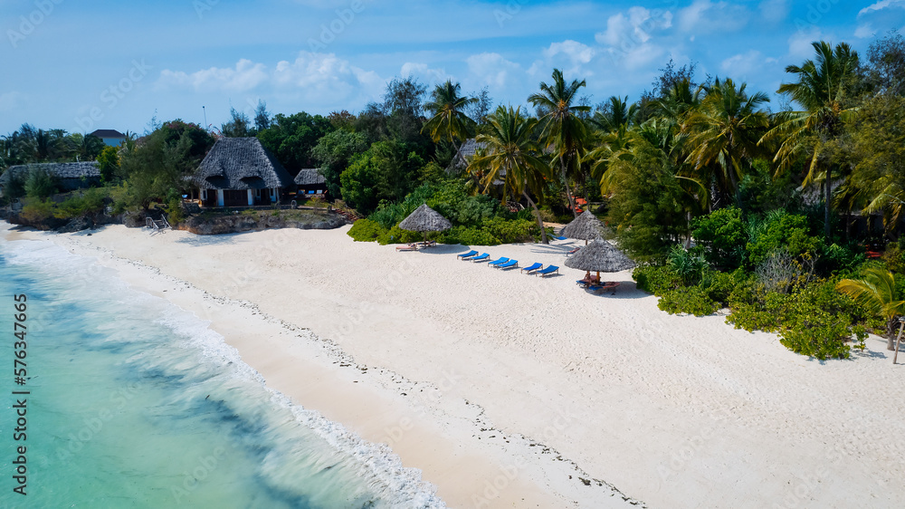 From above, the stunning beauty of Zanzibar's Nungwi Beach is captured in an aerial view with a yacht and palm trees on the sandy beach.