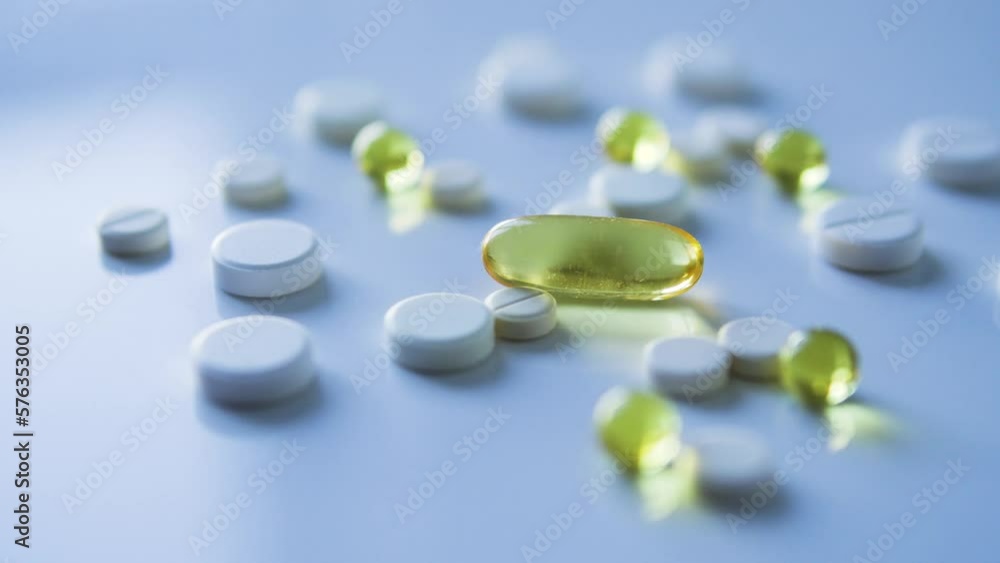 Many white and yellow tablets spilling out of packages lying on rotating table, medicine, medical insurance or pharmacy concept, close-up Many white and yellow tablets spilling out of packages lying on rotating table, medicine, medical insurance or pharmacy concept, close-up
