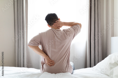 Tired man suffering from back pain at home in bedroom