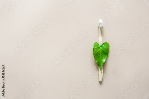 Eine Bambus Zahnbürste mit einem grünen Blatt in Herzform auf einem beigen Hintergrund. Draufsicht.