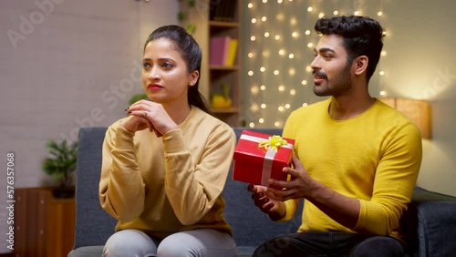 Angry girl rejecting gift from boyfriend while sitting on sofa at home during valentines day celebration - concept of problems, breakup and unhappy.