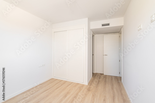 White empty sunny room with built-in wardrobe ventilation and two doors to the bathroom and exit. Concept of a new building or real estate for rent © Pavel