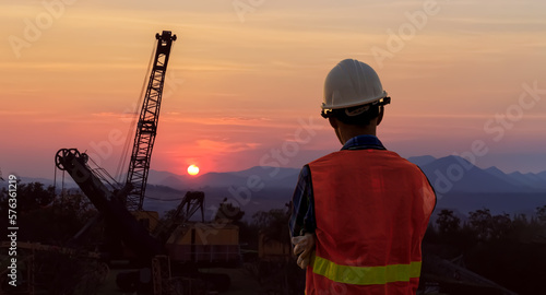 Rear view of a male engineer wearing a white helmet at a job site at dusk