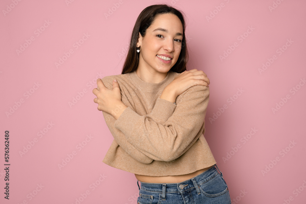 Young beautiful brunette woman wearing casual sweater standing over pink background Hugging oneself happy and positive, smiling confident. Self love and self care Young beautiful brunette woman wearing casual sweater standing over pink background Hugging oneself happy and positive, smiling confident. Self love and self care