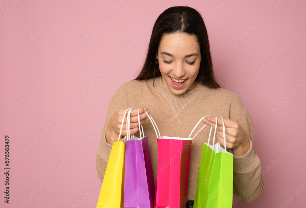 Close-up portrait of cheerful young girl looking into the shopping bags feeling excited isolated on pink background